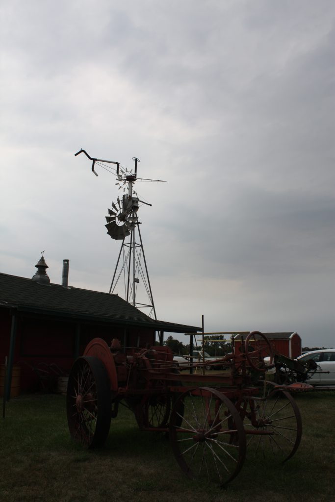 Windmill with horse wind vane and horsedrawn farm equipment in the foreground